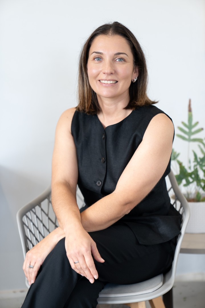 Woman in black outfit seated indoors smiling