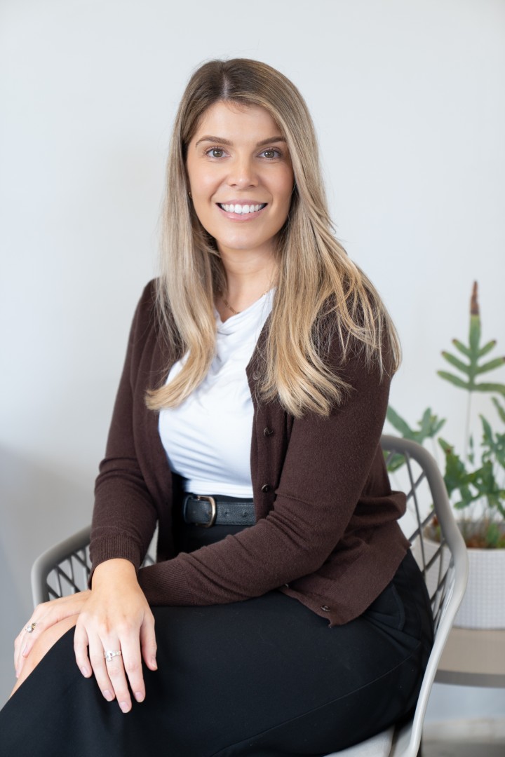 Mia - Smiling woman seated indoors with plant backdrop