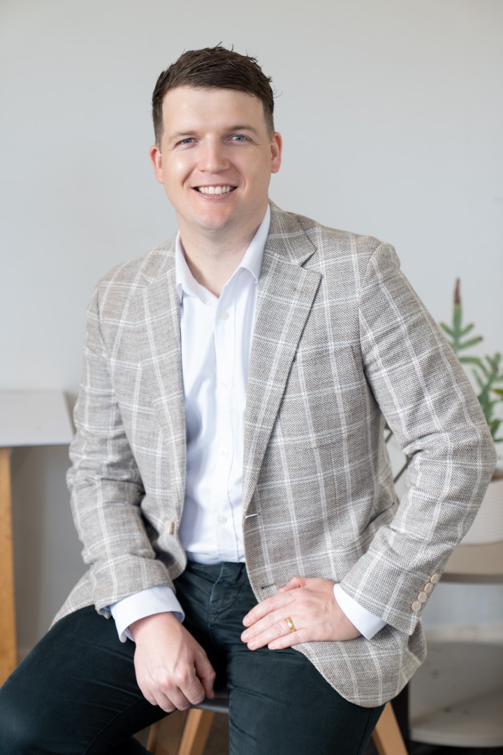 Smiling man in check blazer seated indoors